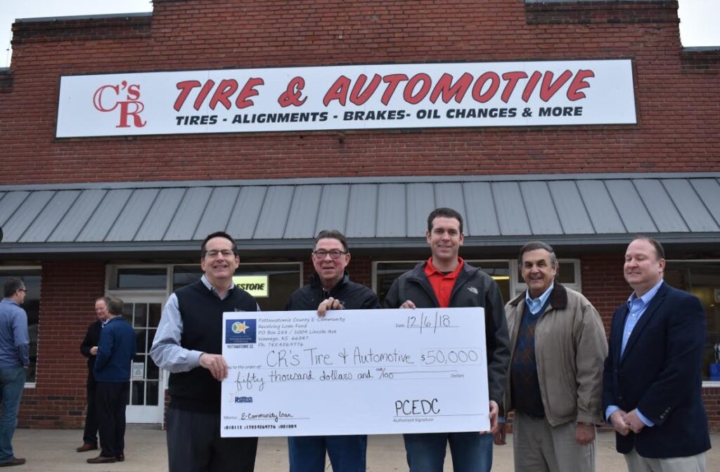 Group photo in font of CR's Tire & Automotive in Wamego, KS, with E-Community Loan check.